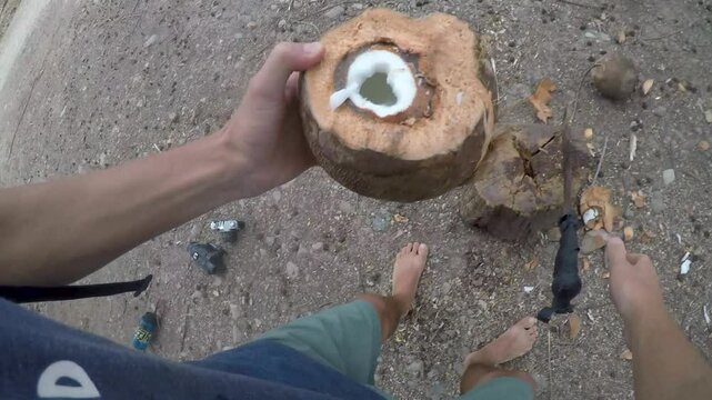 POV of a man poking a hole in the top of a coconut with a machete and looking at the coconut water inside