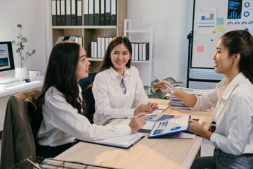 Three young businesswomen are sitting at a table in a modern office, analyzing financial charts and graphs, engaging in a productive discussion about business strategies and performance