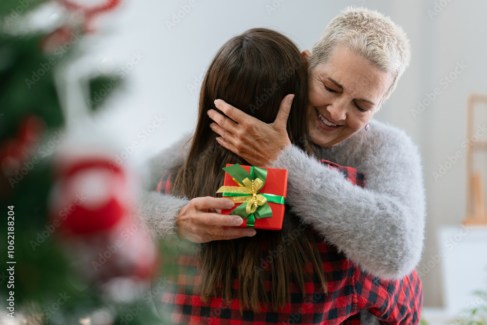 Wall mural Thankful Caucasian woman with christmas gift hugging daughter at home