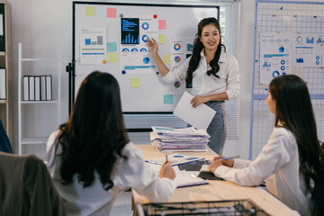 Asian businesswoman leads a meeting in the office, presenting charts and statistics on a whiteboard...