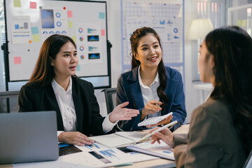 Three asian businesswomen are discussing financial charts and data during a productive meeting in a modern office, collaborating on important business decisions