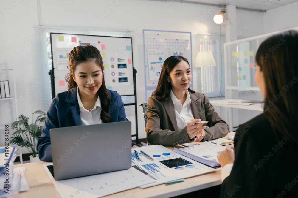 Poster three asian businesswomen are sitting at a desk in a modern office, collaborating on a project using