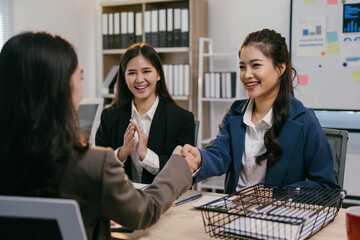 Two businesswomen happily shaking hands in a modern office after a successful job interview, exuding confidence and professionalism. The bright setting reflects teamwork and success