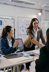 Businesswomen shaking hands celebrating successful agreement in modern office with charts and graphs, colleagues clapping hands in the background