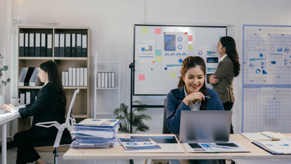 Asian businesswomen are analyzing financial charts on laptop computer and whiteboard, collaborating and brainstorming for successful business strategy in modern office meeting room