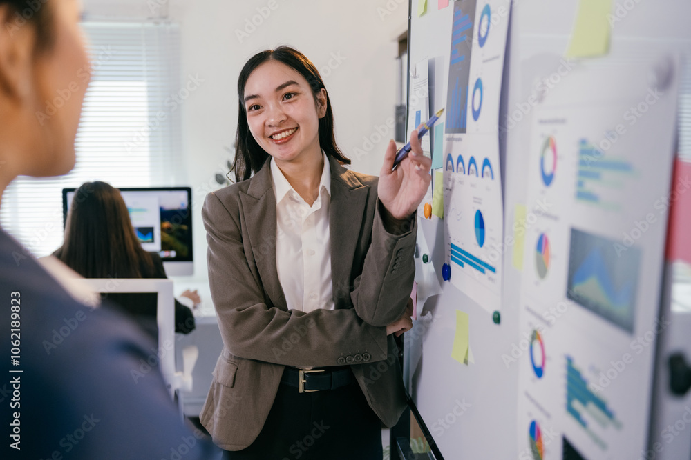 Poster smiling businesswoman pointing at charts and graphs on whiteboard while discussing marketing strateg