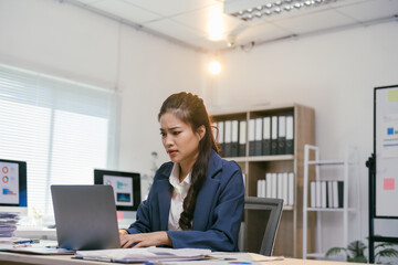 Young asian businesswoman looking stressed while working on a laptop in a modern office, dealing...