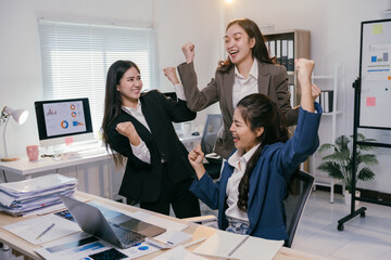 Three joyful businesswomen are raising their arms in celebration of achieving a successful project outcome, expressing their happiness and teamwork in a contemporary office setting
