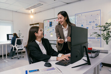 Two cheerful businesswomen are working together on a computer, discussing strategies and analyzing data in a bright, modern office environment, fostering teamwork and collaboration