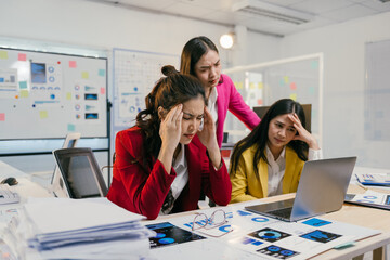 Asian businesswomen are having a headache from overwork and stress about the company's performance, business problem, and financial problem while working in the office