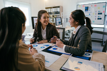 Asian businesswomen are discussing charts and pie graphs during a meeting in a modern office, collaborating on data analysis and financial performance