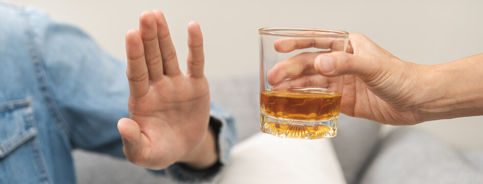 Alcoholism, depressed asian young man refuse, push out alcoholic beverage glass, drink whiskey, sitting alone at night. Treatment of alcohol addiction, having suffer abuse problem alcoholism concept.