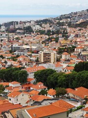 Fototapeta premium A captivating view includes modern high-rises combining with traditional structures scattered across a hilly cityscape, under a cloudy sky, showing urban diversity - Funchal, Madeira, Portugal.