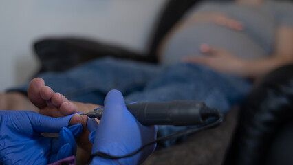 Pregnant woman on a hardware pedicure procedure in a beauty salon. 