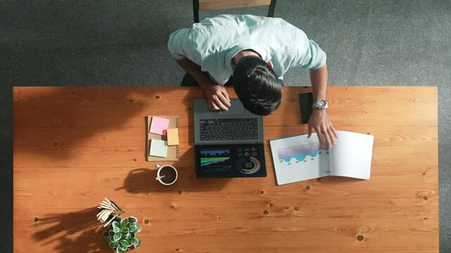 Top aerial view of manager working on laptop while looking at data analysis. Leader compare financial statistic graph while making decision at meeting table with document scatter around. Convocation.