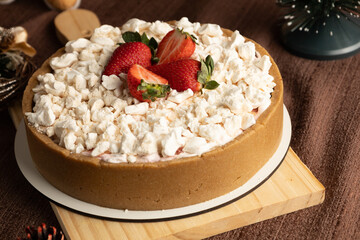 Rustic strawberry meringue tart with a crumbly cookie crust, topped with crushed meringue and fresh strawberries, set in a festive holiday setting with pinecones and Christmas ornaments.
