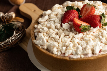 Rustic strawberry meringue tart with a crumbly cookie crust, topped with crushed meringue and fresh strawberries, set in a festive holiday setting with pinecones and Christmas ornaments.
