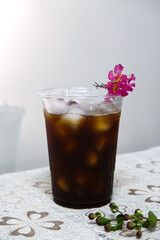 Iced coffee glass with pink flower placed on top with natural light. Front view iced coffee plastic cup for summer. Concept of takeaway, cold drink packaging, coffee, energy, and relaxing at a cafe.