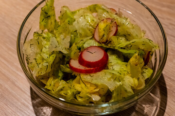 bowl of salad with radishes and lettuce. The salad is in a glass bowl and is on a wooden table