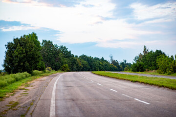 A picturesque asphalt road winds through lush green trees, inviting travelers into a serene natural landscape. Perfect for themes of adventure, travel, or nature exploration.