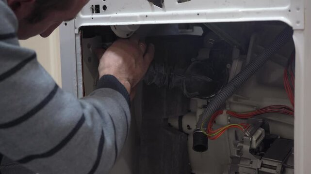 a man repairs a washing machine, the man disconnects the hose in the washing machine