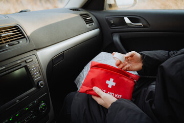 An individual is seated comfortably inside a car, securely holding a first aid kit, indicating...