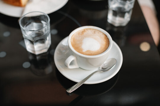 Close-up of a cappuccino and a glass of water on a table at an outdoor caf&eacute;