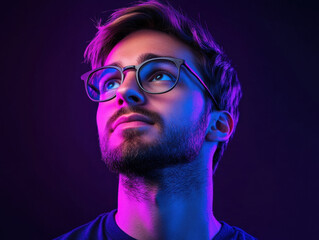 A young man with glasses gazes thoughtfully in vibrant purple and blue lighting, deep in reflection