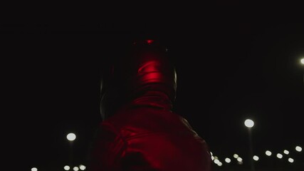 Biker in black helmet sits on his motorcycle in night parking in glare of red light. Slow motion. Circular camera movement. Main advantage of using motorcycle in city is saving time and money