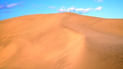 Majestic golden dune top with blue sky and isolated white clouds