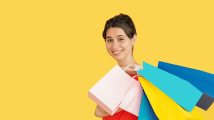 Smiling woman holds shopping bags in bright colors illustrating joyful retail therapy isolated on yellow empty space background.