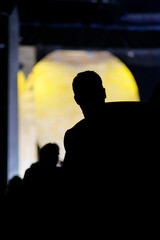 Silhouette of a person standing in a dimly lit space with a bright yellow background during an evening gathering