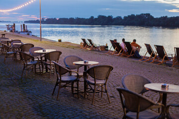 Relaxing evening by the waterfront with chairs, tables, and glowing lights near the calm water