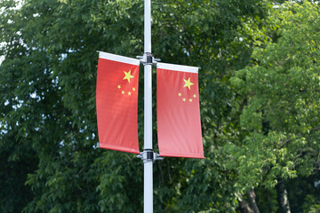 Two Chinese flags displayed on a pole surrounded by lush greenery in a public area during the...