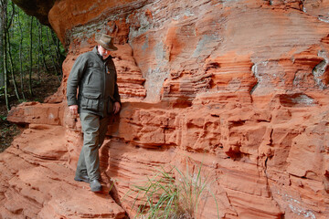 A hiker walks on a narrow path on a steep sandstone wall. The reddish rock face rises impressively beside him, creating a spectacular backdrop for outdoor adventure.