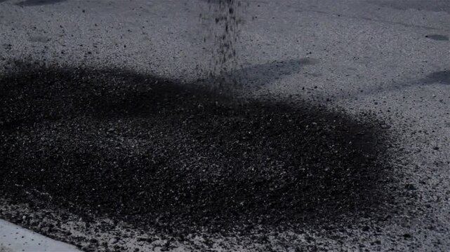 Asphalting, pothole repair. Street resurfacing. Fresh asphalt construction. Bad road. A professional worker of a road company covers a pothole on the road with hot asphalt.