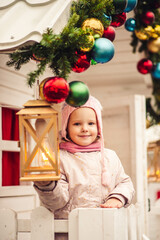 portrait of a girl on the street, the girl is warmly dressed, in a hat and jacket, around her are New Year's decorations, garlands and a lantern