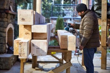 a man grinds wooden beams on the street with a hand sander 