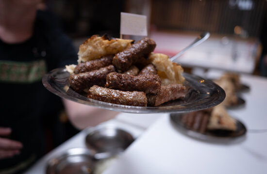 Close-up of a man in a restaurant serving a plate of traditional Balkan meat cevapi (sausage) and bread