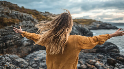 Woman with outstretched arms enjoying the wind and breathing fresh air on the rocky beach