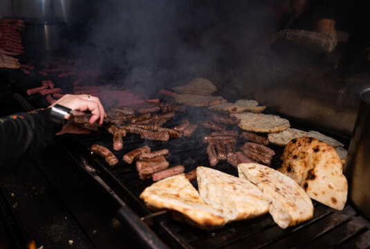 Close-up of a man cooking traditional Balkan meat cevapi (sausage) and bread on a grill