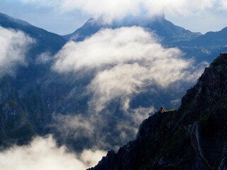 A stunning misty mountain peak emerges through layers of flowing white clouds, creating a sense of mystery and grandeur against the distant blue range - Pico do Arieiro, Madeira, Portugal.