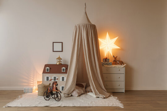 Close-up of a horse toy in front of a doll's house, tent teepee and chest of drawers with wrapped gifts in a child's bedroom