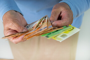 A close-up shot of two hands holding a stack of euro bills. The hands are likely those of an older...