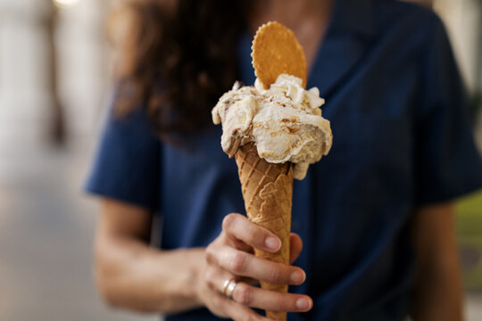 Woman standing in the street holding a waffle Cone with Pistachio and Stracciatella gelato, whipped cream and cookie, Amalfi Coast, Italy