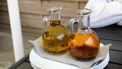 Two glass bottles of infused olive oil with herbs on a restaurant table, rustic Mediterranean setting, natural light, close-up shot, culinary seasoning, dining table decor, gourmet ingredient display