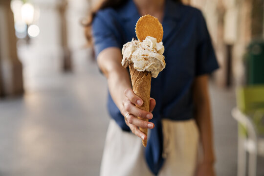 Woman standing in the street holding a waffle Cone with Pistachio and Stracciatella gelato, whipped cream and cookie, Amalfi Coast, Italy
