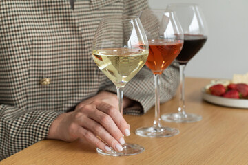 Wine tasting. Three glasses with white, rose and red wine in the hands of a woman on a wooden table