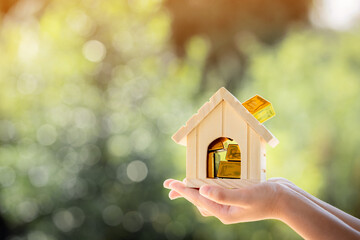 Man hand hold the home and gold bar with work capital management in the public park, Saving money for real estate and loan for buy house investment concept.