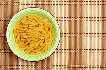 Raw Penne Pasta in Green Bowl on Bamboo Mat
